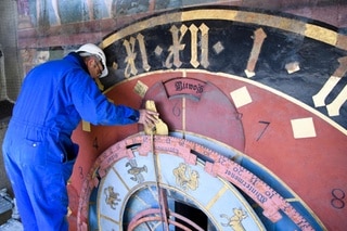 A workman with bis hand on the big hand while inspecting the clock face of the Zytglogge.
