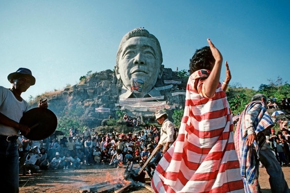 Campesinos filipinos bailando frente al enorme monumento a Ferdinand Marcos