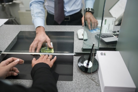 Pessoa entrega notas bancárias em um balcão bancário